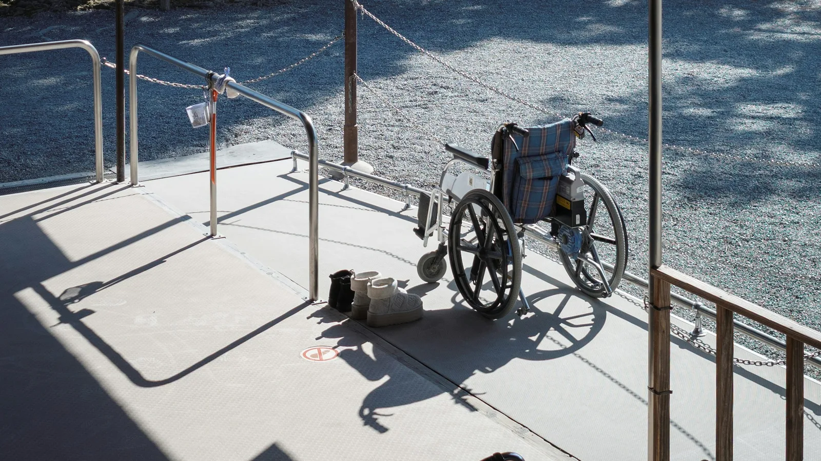 A wheelchair beside a ramp and handrails at a covered entrance