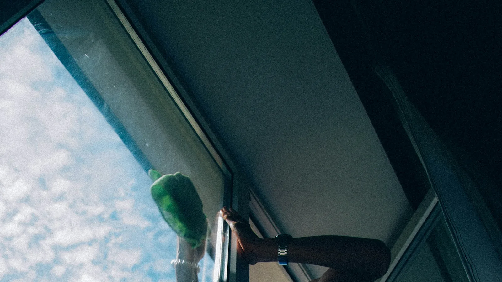 A person wiping a window with a green cleaning cloth