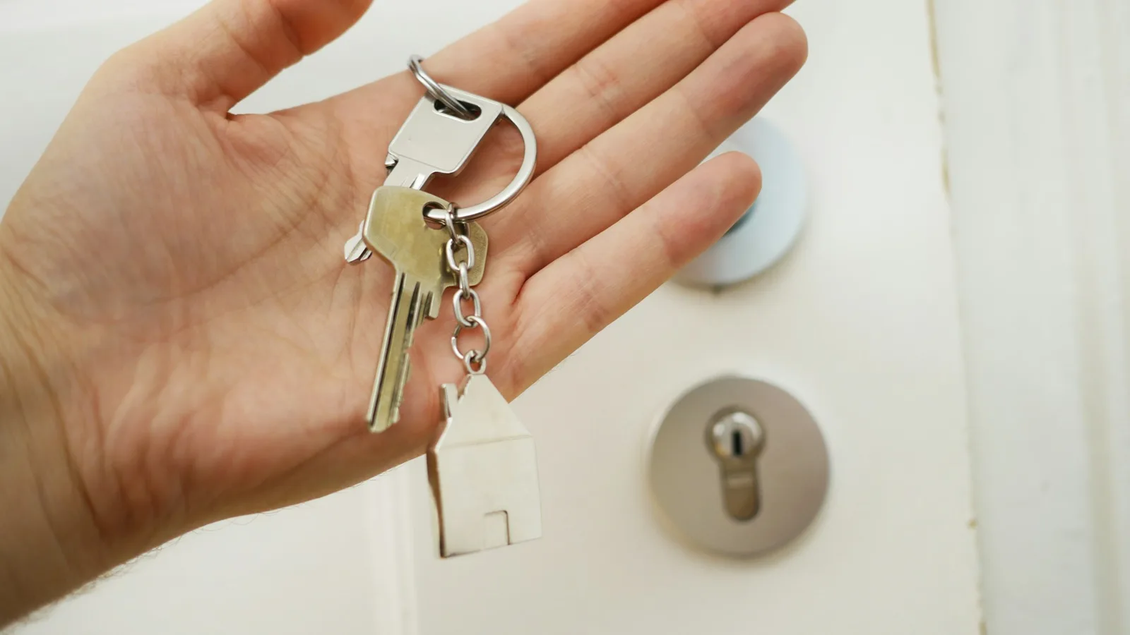 A hand holding house keys beside a door lock